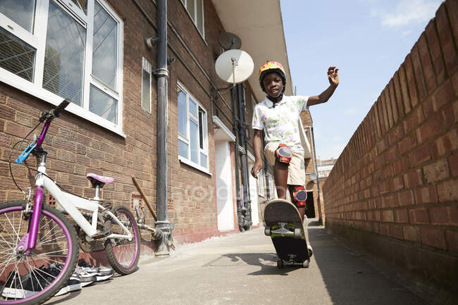 Portrait carefree boy skateboarding in sunny apartment alleyway — Stock Photo