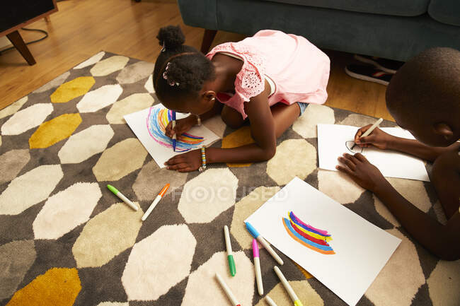 Chica dibujo multicolor arco iris con marcadores en la alfombra de la sala de estar - foto de stock