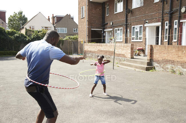 Pai e filha brincando com aros de plástico no bairro ensolarado — Fotografia de Stock