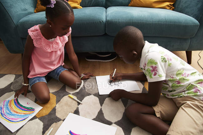 Brother and sister coloring with markers on living room rug — Stock Photo