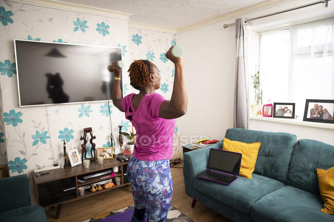 Frau mit Kurzhanteln übt online im Wohnzimmer — Stockfoto