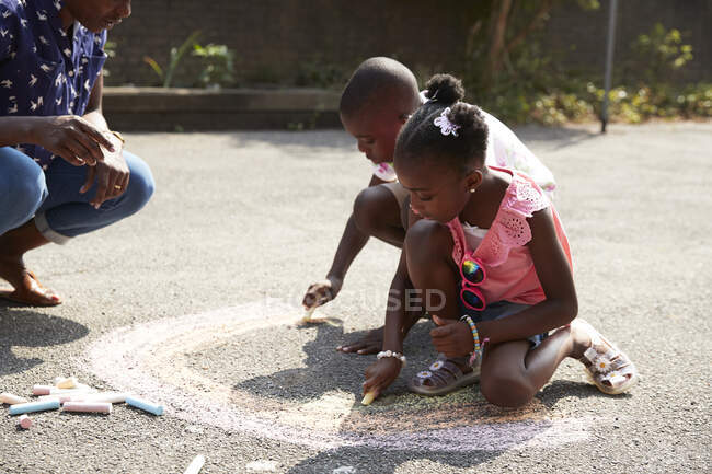 Брат и сестра раскрашивают радугу мелом на солнечном тротуаре — стоковое фото