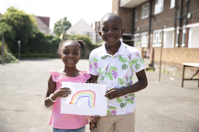 Portrait cute brother and sister holding rainbow drawing outside — Stock Photo