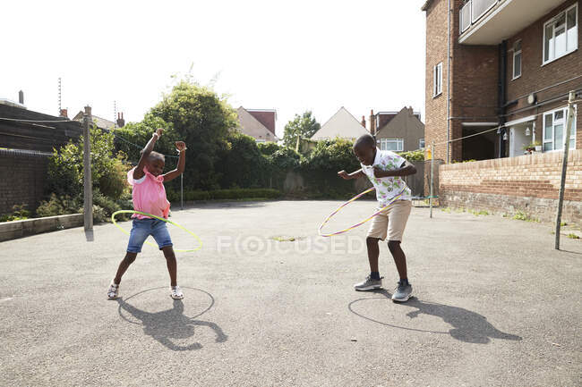 Irmão brincalhão e irmã girando em aros de plástico em lote ensolarado — Fotografia de Stock
