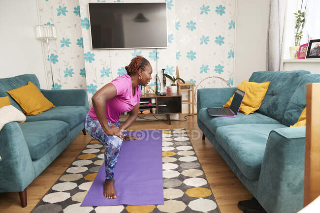 Mulher praticando ioga on-line no laptop na sala de estar — Fotografia de Stock