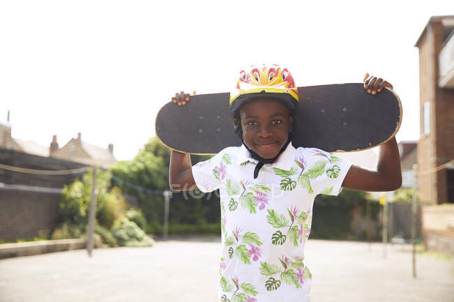 Retrato menino confiante com skate no parque de estacionamento ensolarado — Fotografia de Stock