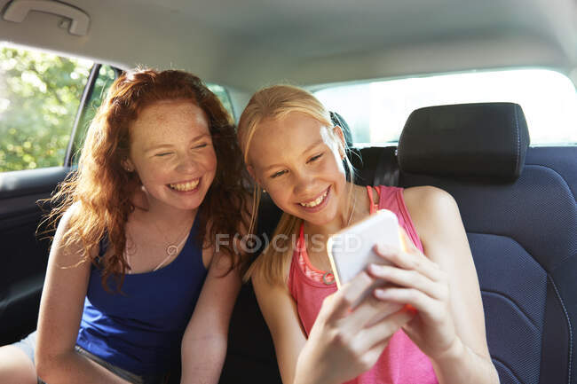 Felices amigas preadolescentes tomando selfie en el asiento trasero del coche - foto de stock
