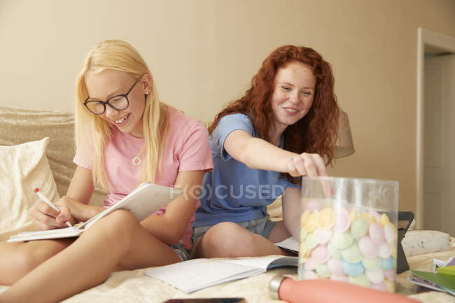 Glücklich preteen mädchen friends eating candy und studying auf bed — Stockfoto