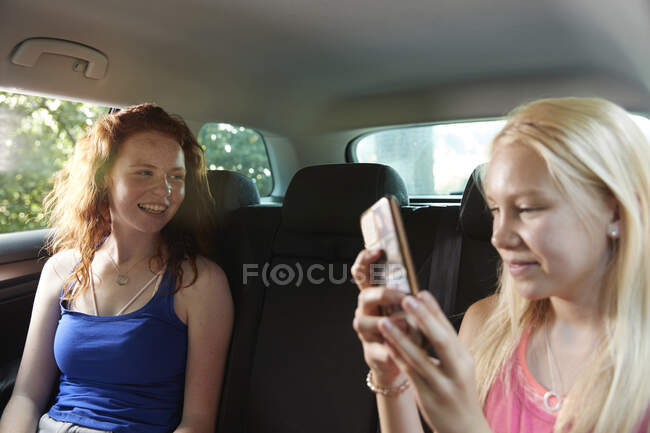 Preteen girl friends using smarphone in back seat of car — стоковое фото