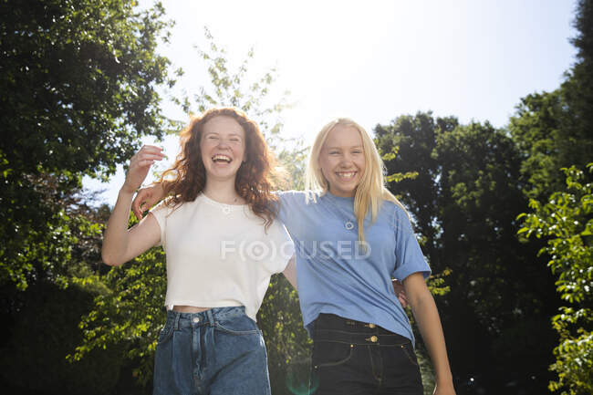 Portrait happy preteen girl friends below sunny summer trees — Stock Photo