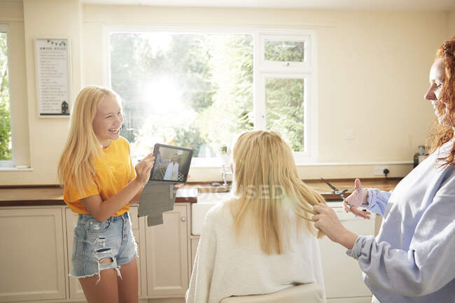 Happy preteen girls with digital tablet cutting mother hair in kitchen — Stock Photo