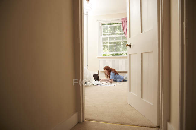 Девочка-подросток выполняет домашнюю работу на ноутбуке на полу спальни — стоковое фото