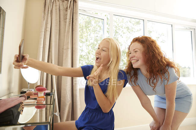 Juguetonas amigas preadolescentes tomando selfie en el dormitorio - foto de stock