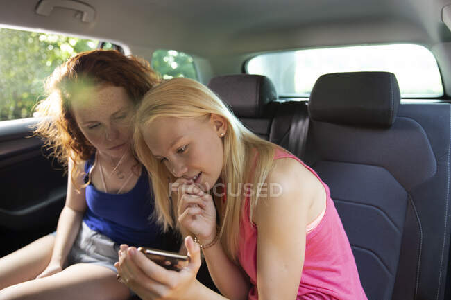 Preteen girl friends using smarphone in back seat of car — стоковое фото