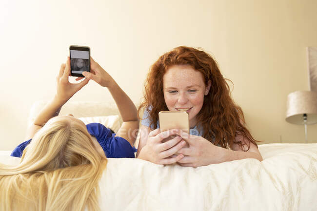 Preteen girls friends using smartphones on bed — Stockfoto
