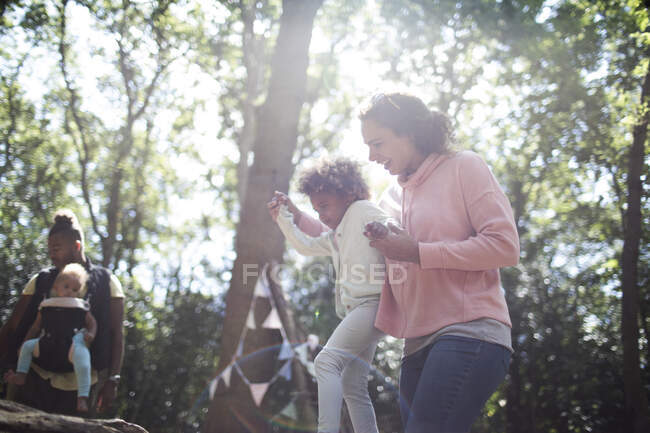 Mãe ajudando filha equilíbrio em tronco caído em bosques ensolarados — Fotografia de Stock