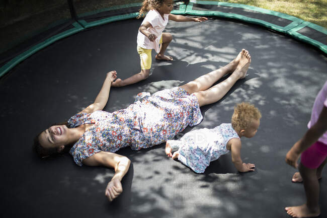 Hijas jugando alrededor despreocupada madre tendida en trampolín - foto de stock