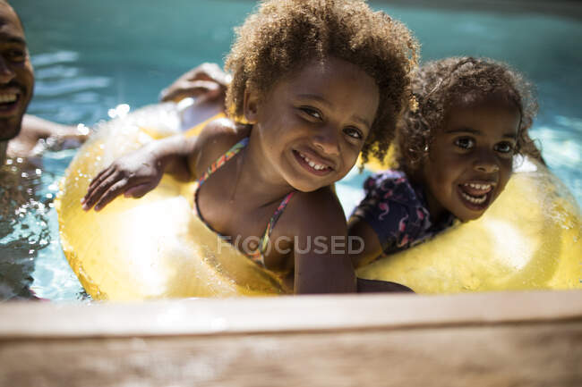 Portrait happy sisters in inflatable ring in sunny swimming pool — Stock Photo