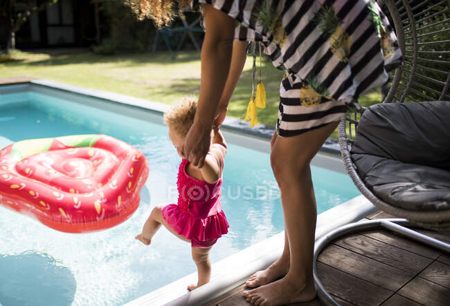 Madre ayudando a su hija pequeña en la piscina de verano - foto de stock