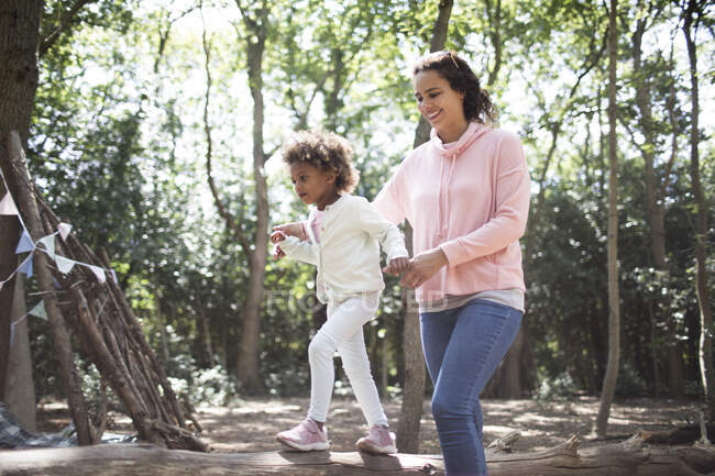 Mother helping daughter walk on fallen log in sunny woods — Stock Photo
