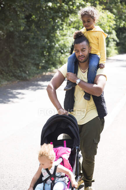 Père portant et poussant sa fille en poussette sur un chemin ensoleillé — Photo de stock