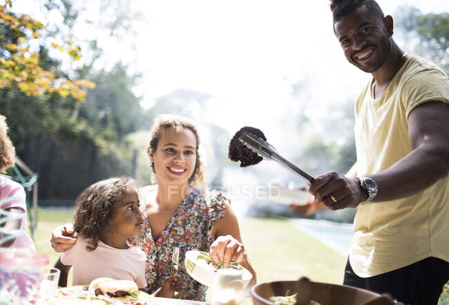 Retrato feliz familia disfrutando de barbacoa en patio trasero soleado - foto de stock