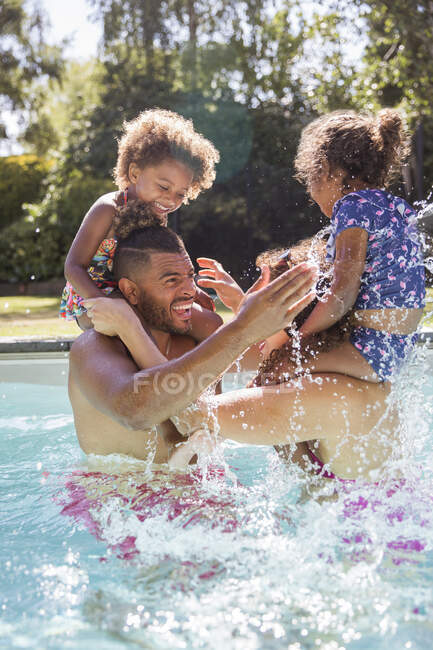 Padres e hijas juguetonas jugando al pollo en la piscina soleada - foto de stock