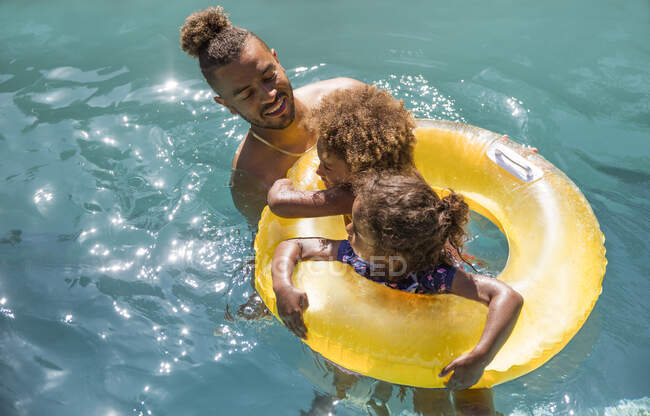 Padre e figlie in anello gonfiabile nella soleggiata piscina estiva — Foto stock