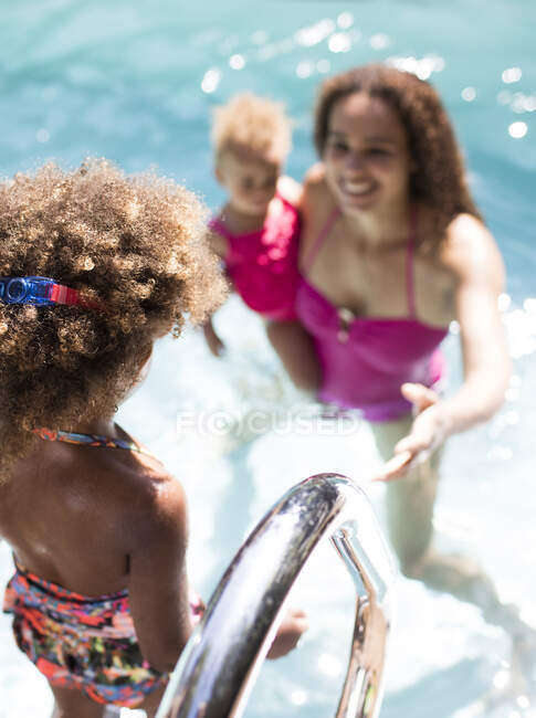 Madre viendo hija entrar en la piscina soleada de verano - foto de stock