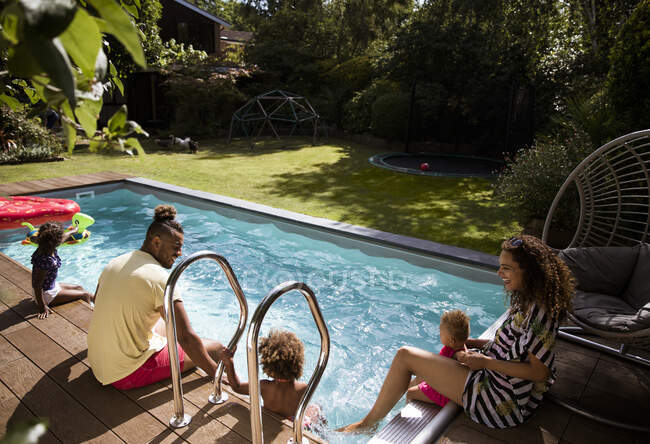 Familia feliz relajándose en el soleado patio de verano junto a la piscina - foto de stock