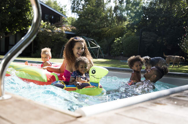 Família feliz jogando na piscina ensolarada de verão — Fotografia de Stock