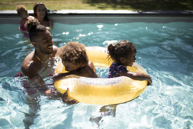 Famille jouant avec l'anneau gonflable dans la piscine ensoleillée d'été — Photo de stock