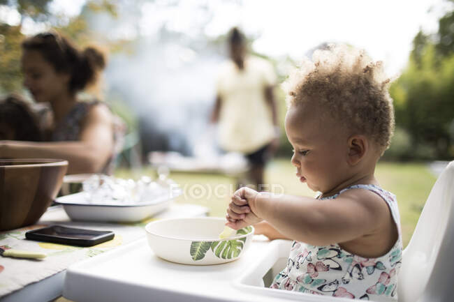 Toddler girl eating in high chair on summer patio — Stock Photo
