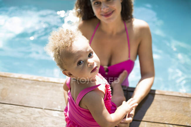Portrait cute toddler daughter with mother at sunny swimming pool edge — Stock Photo