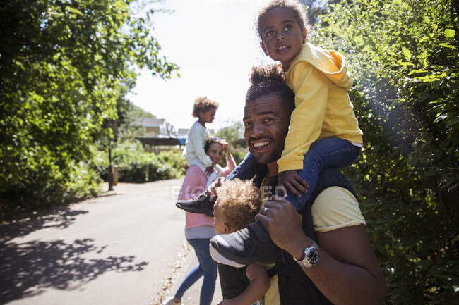 Porträt glücklicher Vater trägt Töchter auf sonnigem Bürgersteig — Stockfoto