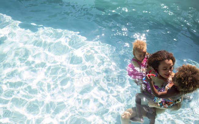 Madre e hijas en la soleada piscina de verano - foto de stock
