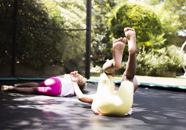 Carefree sisters laying on sunny backyard trampoline — Stock Photo