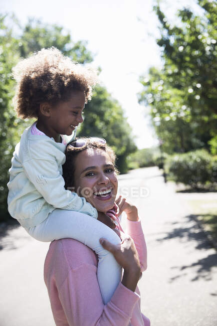 Portrait happy mother carrying daughter on shoulders in sunny street — Stock Photo