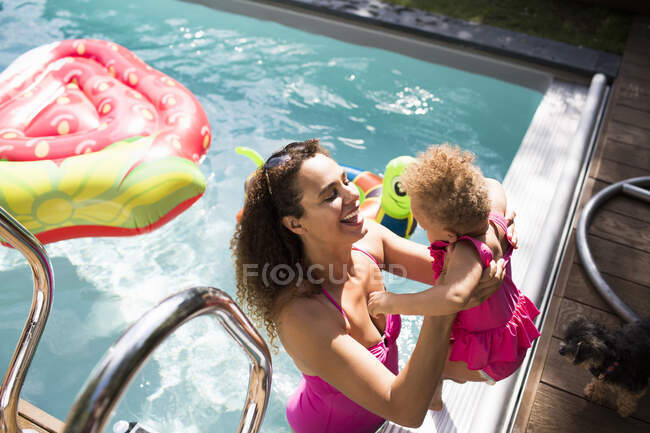 Happy mother lifting daughter into sunny summer swimming pool — Stock Photo