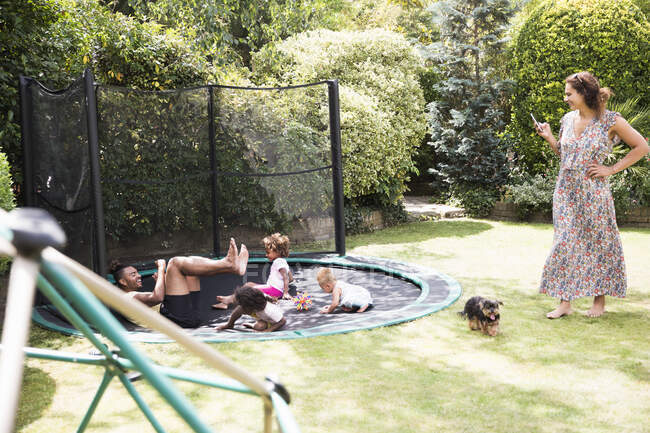 Família jogando no ensolarado trampolim quintal — Fotografia de Stock