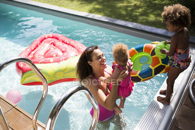 Madre e hijas jugando en la soleada piscina de verano - foto de stock