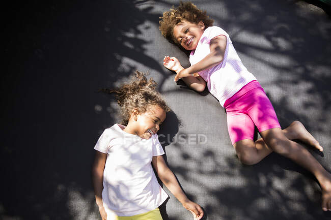 Happy cute sisters laying on sunny trampoline — Stock Photo