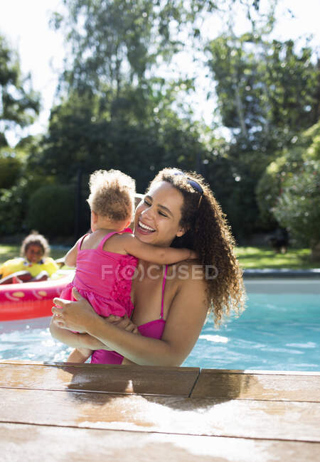 Happy mother holding daughter in sunny summer swimming pool — Stock Photo
