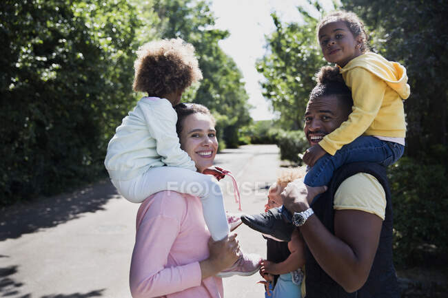 Portrait happy couple carrying daughters on shoulders on sunny road — Stock Photo