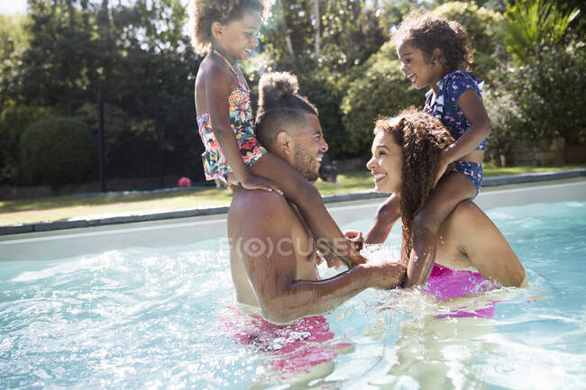 Genitori giocosi che giocano al pollo con le figlie sulle spalle in piscina — Foto stock
