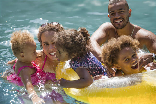 Retrato familia feliz jugando en la soleada piscina de verano - foto de stock
