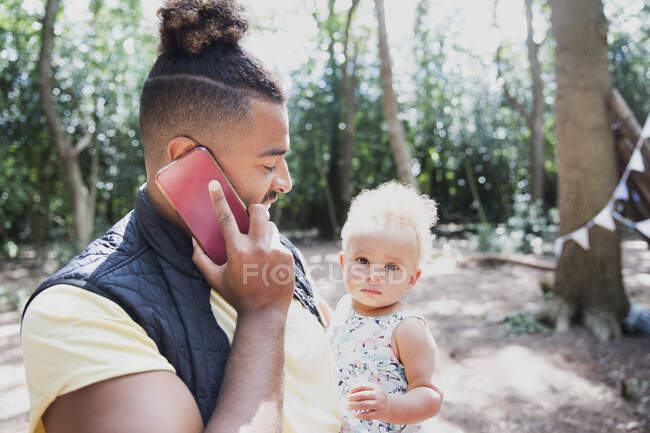 Father holding toddler daughter and talking on smart phone in woods — Stock Photo