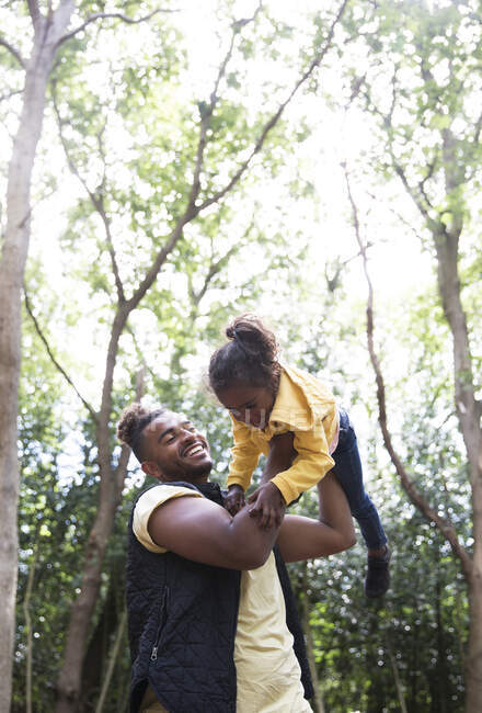 Playful daughter flying daughter under trees in park — Stock Photo