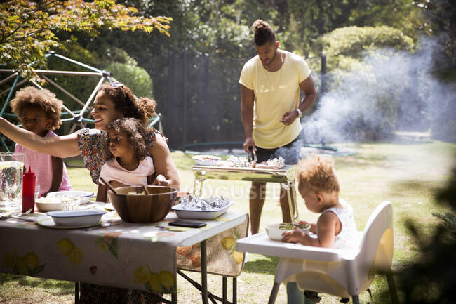 Family barbecuing and eating on sunny summer backyard patio — Stock Photo