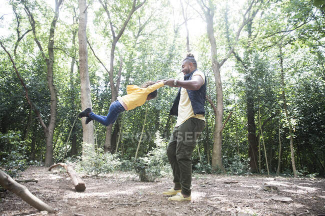 Playful father swinging daughter below trees in sunny woods — Stock Photo